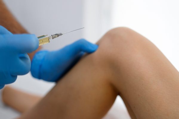 Close up view of doctor hands with syringe injecting into a inflamed knee